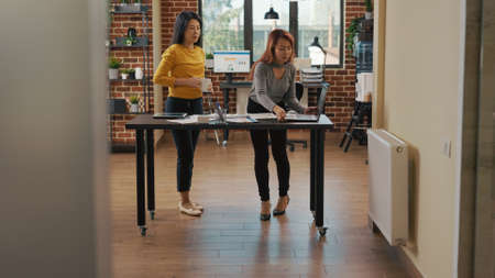 Office workers pointing at laptop to create management project for business growth. Colleagues doing teamwork to plan marketing application for financial investment at startup job.の写真素材