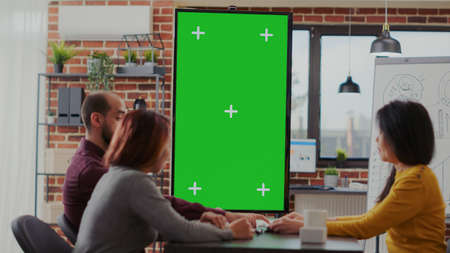 Coworkers meeting in office with green screen on monitor vertically to plan business strategy. Diverse team of people looking at mockup copy space with isolated template and chroma key.の写真素材