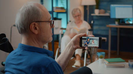 Retired man talking to daughter and niece in hospital on video call, sitting next to crutches....