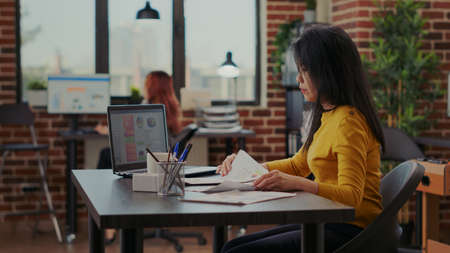 Consultant analyzing financial paperwork with sales graphs, working with laptop to develop marketing presentation for economy growth. Business woman creating successful strategy.の写真素材