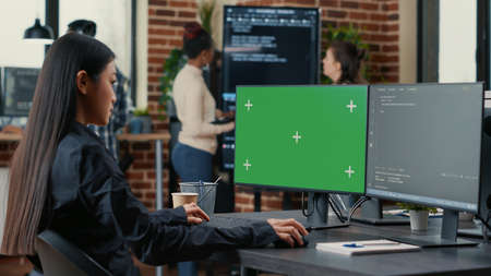 Asian programer writing code in front of computer with green screen chroma key mockup in software...