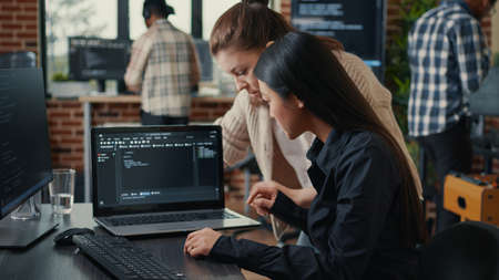 Team of software developers talking about source code running on laptop screen while sitting at desk artificial intelligence server room. Database admins collaborating on data coding group project.の写真素材