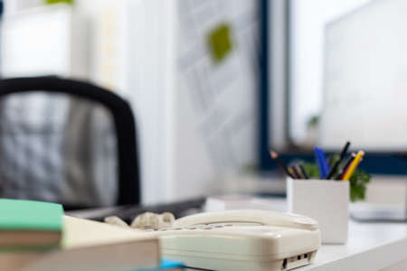 Closeup of phone on desk in empty business office. Startup workspace furniture in indoors work...