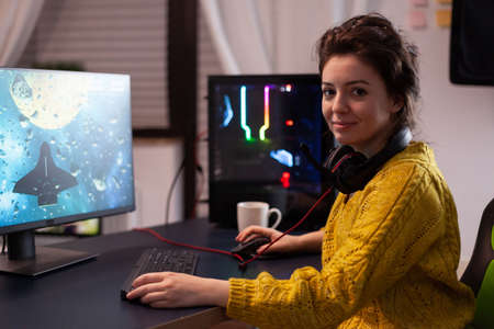 Portrait of focused woman gamer looking into camera while playing space shooter vidogames during online championship using RGB powerful computer in gaming studio. Esport competitionの写真素材