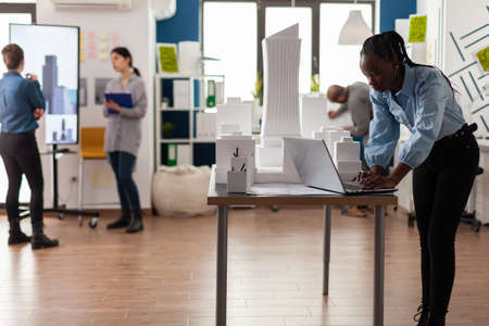 Architect in modern achitectural office working on laptop at desk with 3d white foam scale model of...