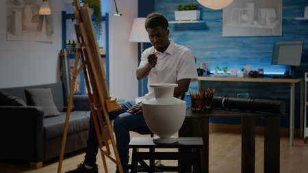 Artist of african american ethnicity analyzing vase for creative drawing sitting in workshop studio. Black adult with artistic imagination using inspiration for successful masterpieceの写真素材