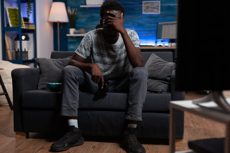 Sad upset cyber player playing video games on television using gaming controller losing online competition. Pro gamer making loser gesture, lying on sofa enjoying fun activity during free timeの写真素材