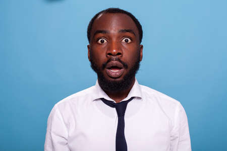 Shocked businessman looking surprised with open mouth facing unbelievable situation on blue background. Amazed person with big eyes jaw dropping. Astonished office worker.の写真素材