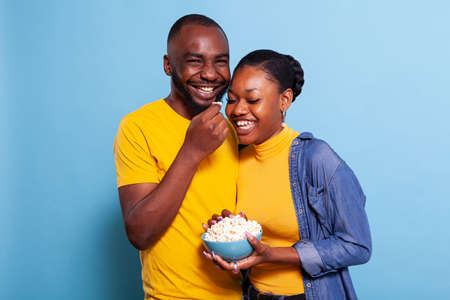 Amused people watching comedy on television and having snack over blue background. Cheerful couple laughing at funny movie, eating popcorn and enjoying millennial activity together.の写真素材
