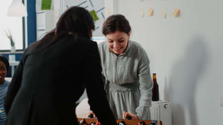 Women having fun while playing with foosball table at office after work. Cheerful colleagues...