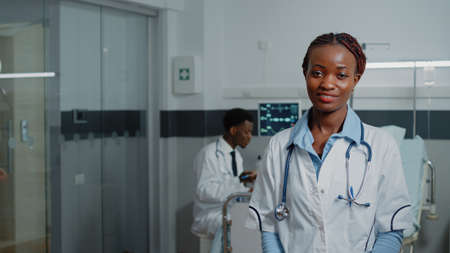 Portrait of african american medic with white coat standing in hospital ward. Confident physician with stethoscope ready to help patient with disease. Healthcare specialist at workの写真素材