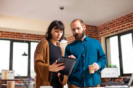 Woman manager holding tablet computer showing company report to entrepreneur man discussing business...