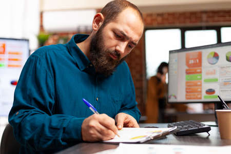Entrepreneur sitting at desk writing marketing strategy analyzing data charts using computer...