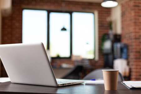 Close up of laptop computer and coffee cup on desk in empty business office. Nobody in modern...