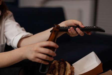 Close-up of caucasian woman hands changing tv stations using black tv remote in living room. Person...