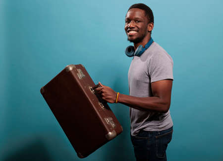 Smiling model holding suitcase baggage to go on trip, leaving on vacation. Young person with retro...