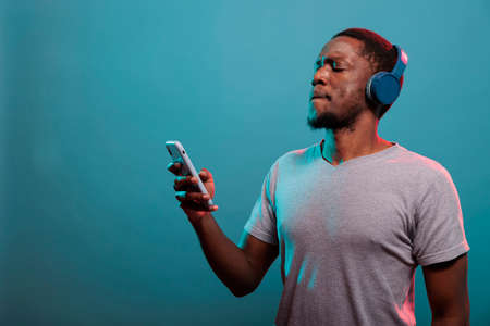 Millennial man using mobile phone and enjoying music on headphones, having fun with mp3 audio sound. Positive adult with smartphone listening to record song on wireless headset.の写真素材