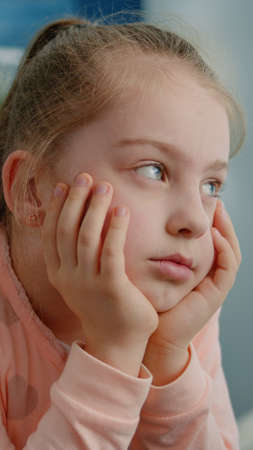 Close up of tired child listening to remote online lesson for school work at home. Exhausted young girl looking at screen for learning and class tasks while sitting at desk, falling asleepの写真素材