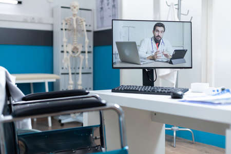 Compute screen with remote doctor talking during online videocall meeting conference standing on table in empty hospital office during consultation. Telemedicine videoconference callの写真素材