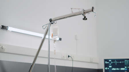 Close up of IV drip bag and empty hospital ward bed. Nobody in emergency room for reanimation and intesive care with heart rate monitor and oxygen tube. Space for healthcare recoveryの写真素材