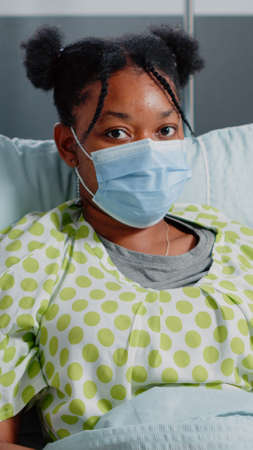 Portrait of young patient with sickness wearing face mask in hospital ward. Sick woman in bed...