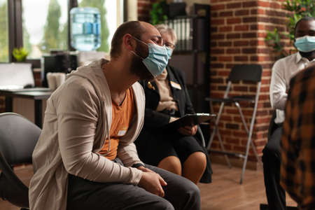 Close up of man having conversation about addiction at aa group meeting with people during coronavorus pandemic. Patients attending therapy session with psychologist, wearing face masks.の写真素材
