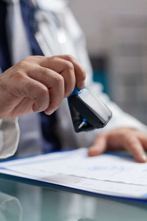 Hand of general practitioner using medical stamp on prescription paper. Health care specialist putting seal on checkup file to give treatment to patient at consultation. Close upの写真素材