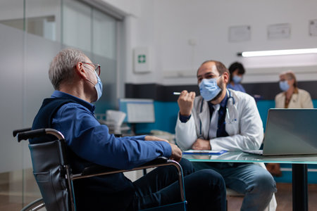 Pensioner sitting in wheelchair at checkup visit with medic during coronavirus pandemic. Doctor...