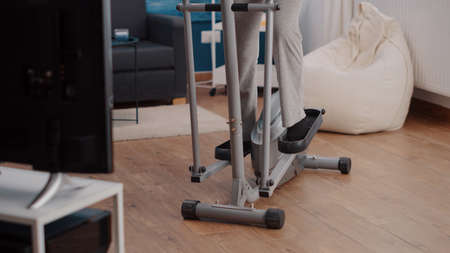 Old person riding stationary bicycle and exercising at home. Aged woman doing cardio training with...