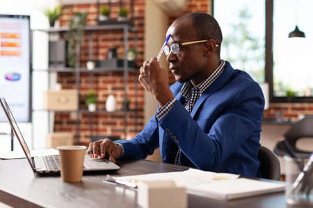 Company worker brainstorming ideas and working on laptop to plan project in office. Business man thinking about solution, planning marketing strategy on computer, feeling pensive.の写真素材