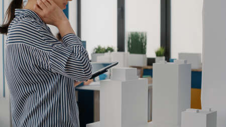 Close up of architect holding tablet and analyzing building model to plan layout. Woman engineer...