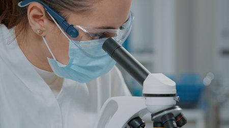 Specialist analyzing dna on microscope in laboratory, wearing face mask, glasses and gloves for...