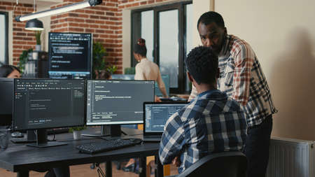 Software developer writing code on laptop and computer keyboard looking at multiple screens with...