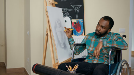 African american man with disability using pencil to draw on canvas, learning new artistic skills in...