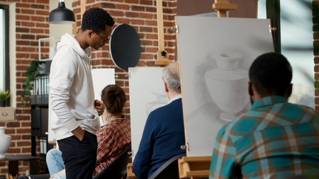 Young man looking at elder student drawing vase model in artistic workshop program to practice art...