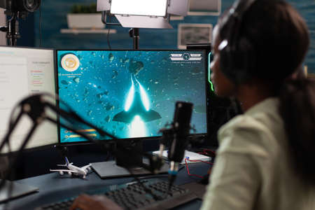 African american pro gamer wearing headset talking with remote players during live streaming using...