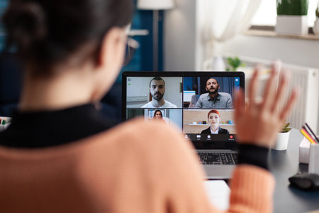 Student in a group videocall on laptop. Freelancer working from home office meeting colleagues online. Colleague waving at screen in webcam team conference. Remote briefing conversation.の写真素材