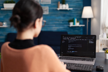 Freelancer programming software on laptop. Programmer working remote from home office. Code tester debugging on laptop using keyboard. Student developer typing data on screen.の写真素材