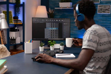 Young architect wearing headphones looking at building structure analyzing prototype on computer...