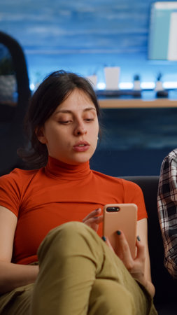 Modern interracial couple using technology on couch at home. Caucasian woman holding smartphone...