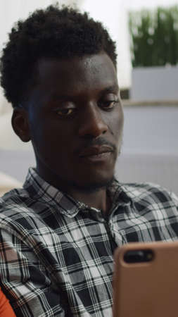 Close up of mixed race couple using smartphone at home in living room. Interracial married people looking at screen device and talking while sitting on couch. Multi ethnic husband and wifeの写真素材