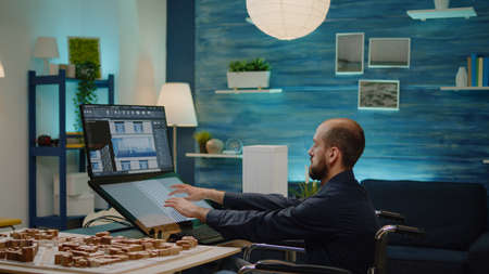 Disabled man working as architect with building model on touch screen monitor at office. Engineer...