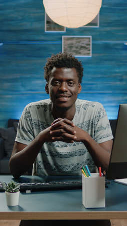 Portrait of black adult sitting at desk with computer and notebook. Man of african ethnicity looking...