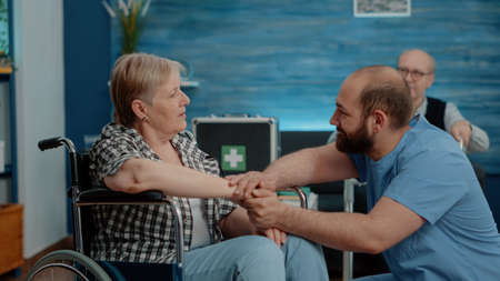 Man nurse holding hands and comforting pensioner with disability in nursing home. Medical assistant...