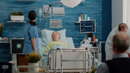 Medical team doing consultation with sick patient in bed at nursing home clinic. Doctor and nurse checking healthcare and treatment with equipment and tools at checkup visit for senior womanの写真素材