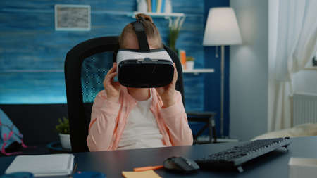 Young girl using vr glasses to learn about virtual reality with modern technology at desk. Little...