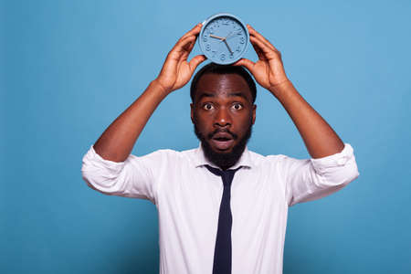 Portrait of stressed office worker holding alarm clock over head showing passing time concept on...