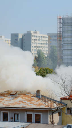 View of firefighters using water to extinguish fire from burning house. Smoke and flames created by...