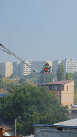 Firemen on platform truck going on building roof to extinguish fire in city. Firefighters on house...