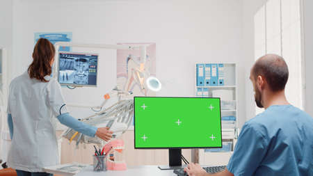 Dental assistant using monitor with horizontal green screen in dentist office. Oral care specialists...